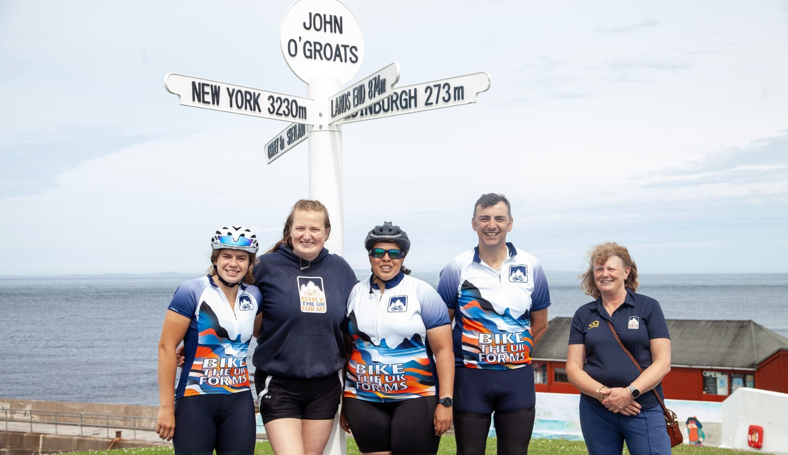 Bike the UK for MS cyclists and route leaders posing in front of the iconic John O'Groats signpost