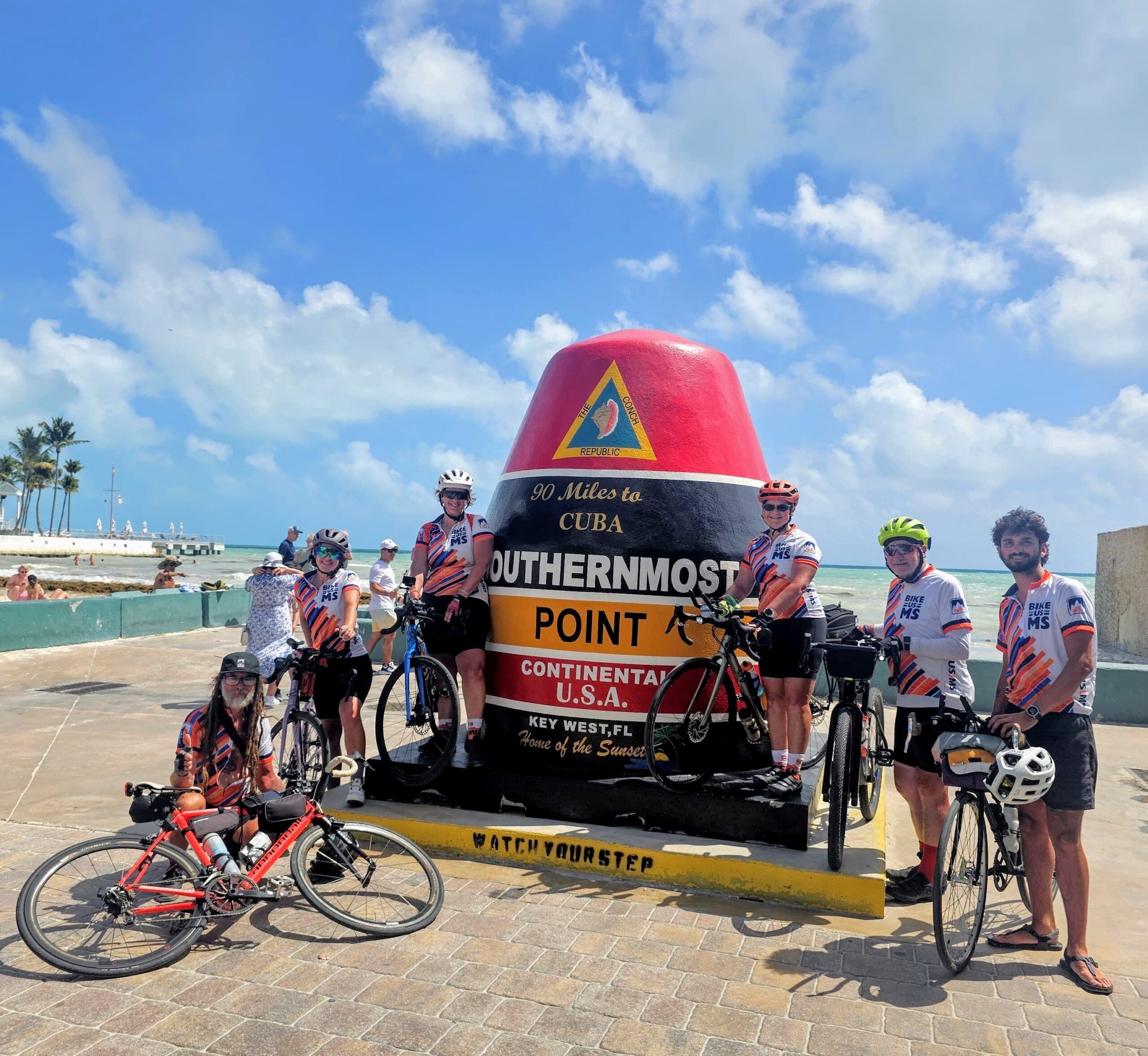 Bike the US for MS cyclists posing next to a statue marker with their bike and team Jerseys at the Southernmost point of continental USA